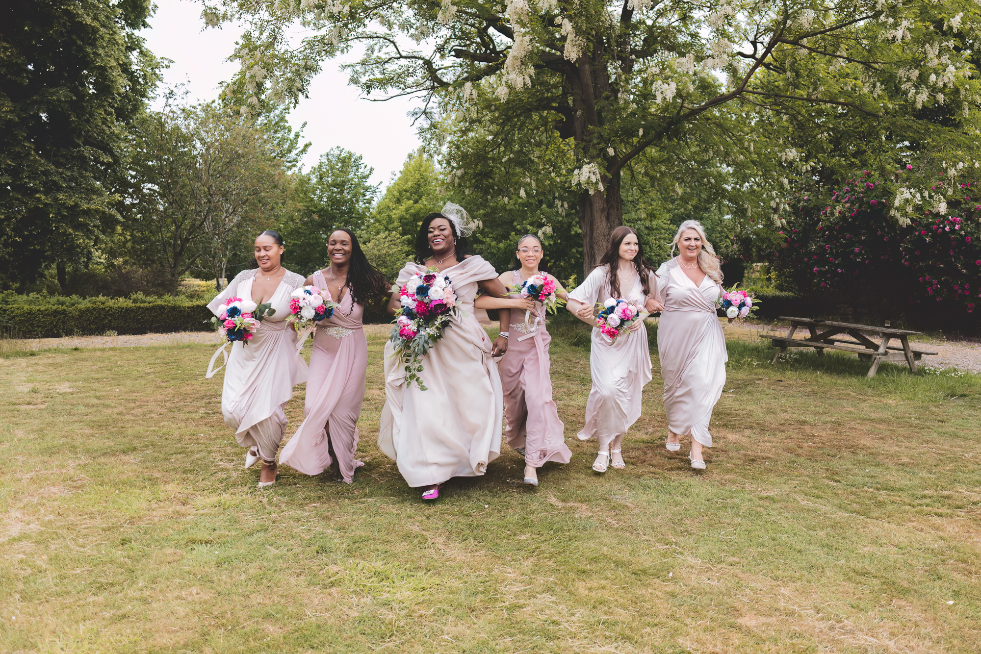 Bride and bridesmaids walking through garden during Yorkshire outdoor wedding celebration  If used on a venue page