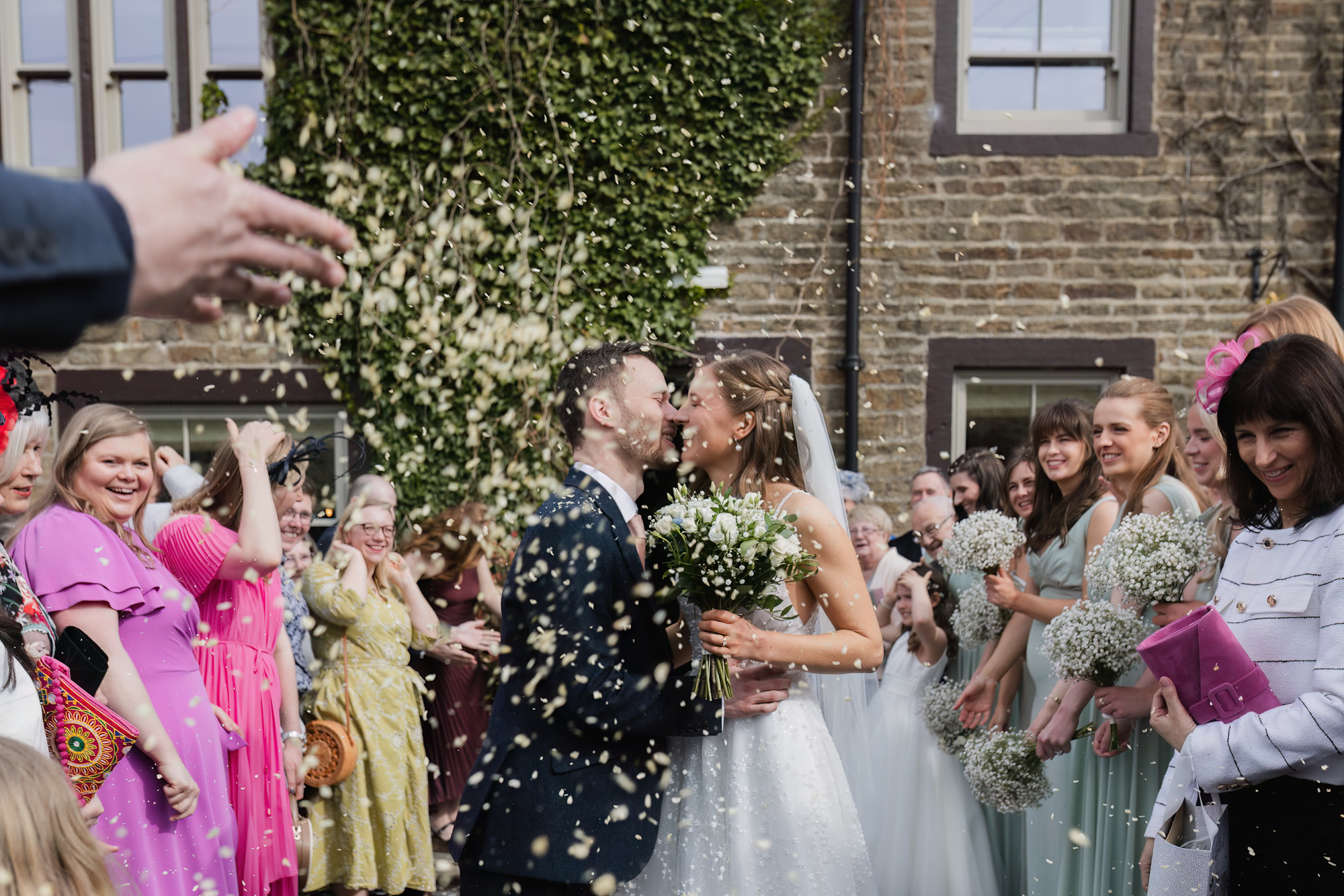 Bride and groom kissing during confetti exit surrounded by guests at a Yorkshire wedding venue