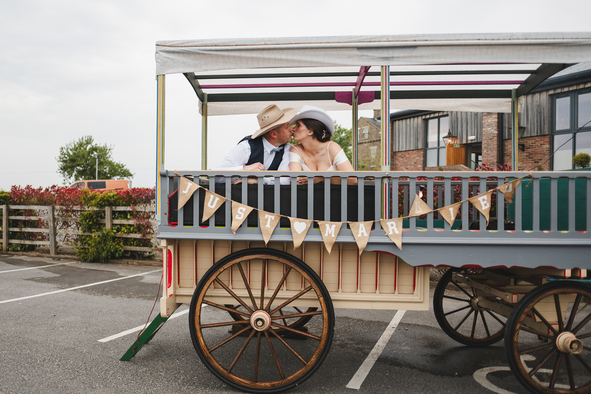 Bride and groom kissing on vintage wedding wagon during rustic countryside wedding reception in Yorkshire UK