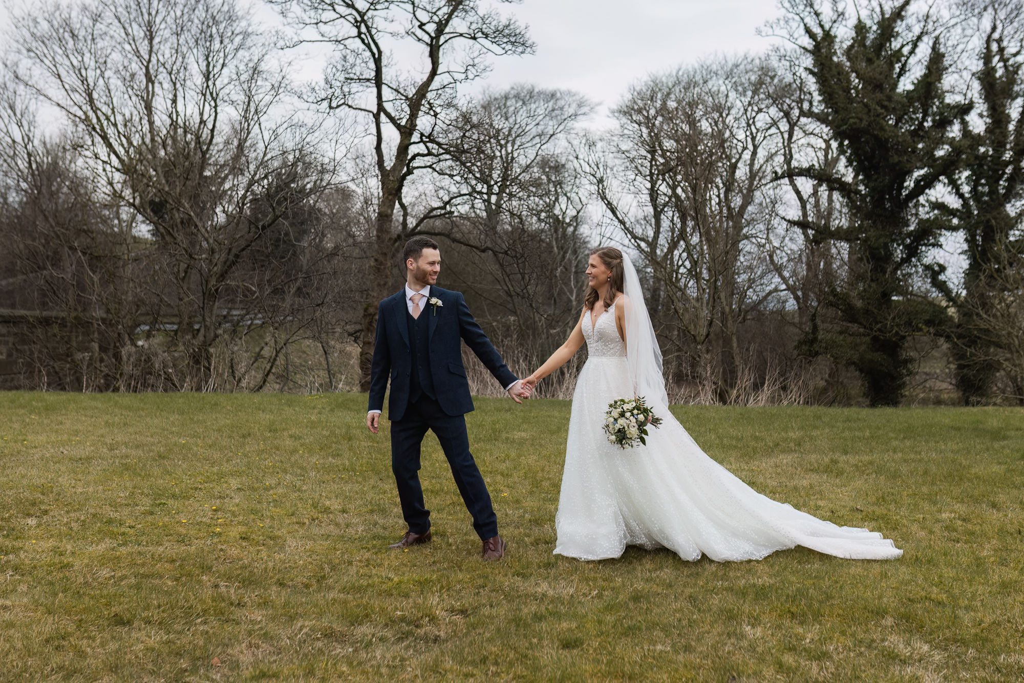 Bride and groom holding hands during relaxed outdoor wedding portraits at a Yorkshire wedding venue  Short Alt Text