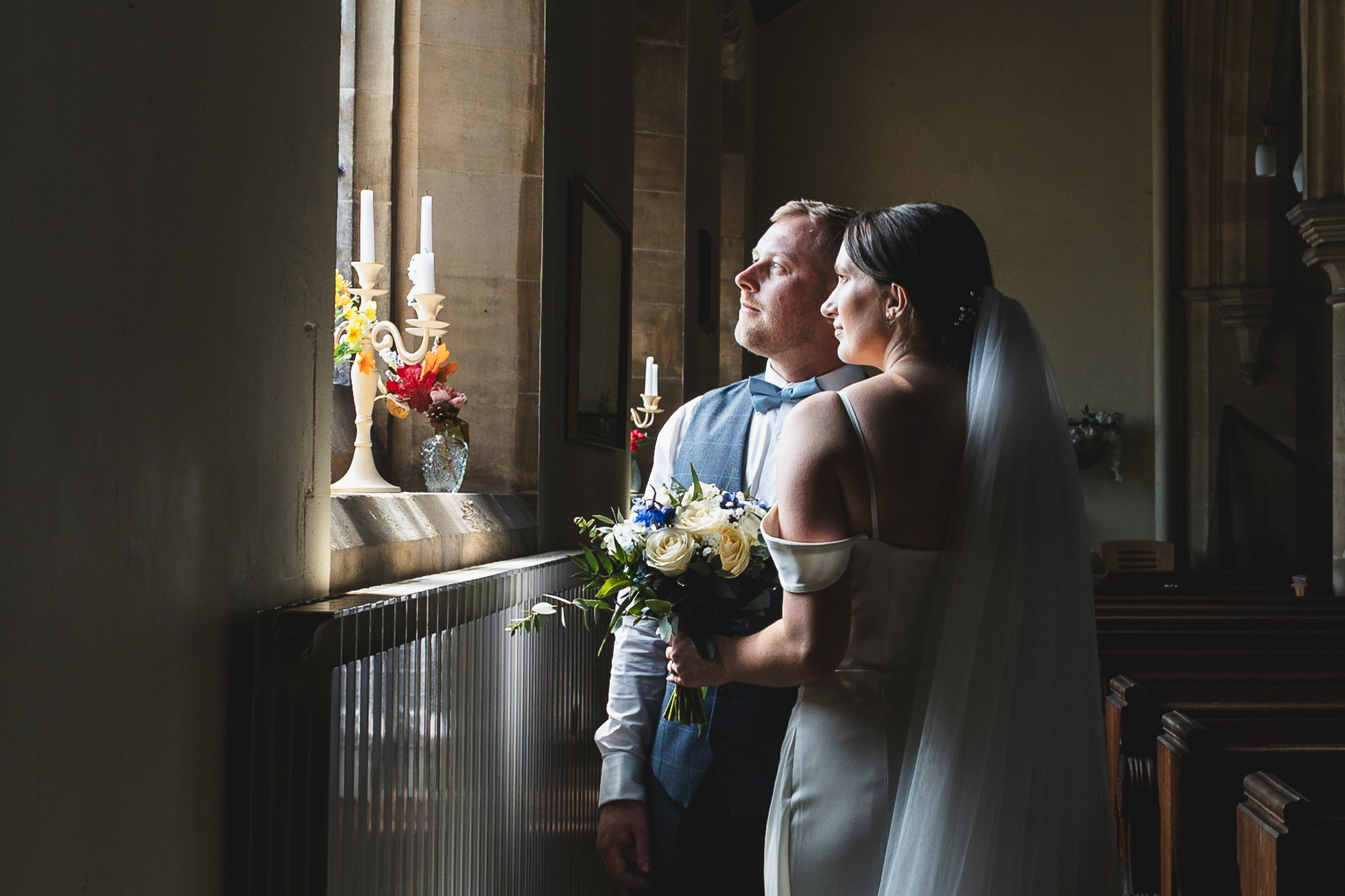 Moody documentary wedding portrait of bride and groom by church window during intimate UK wedding ceremony in Yorkshire