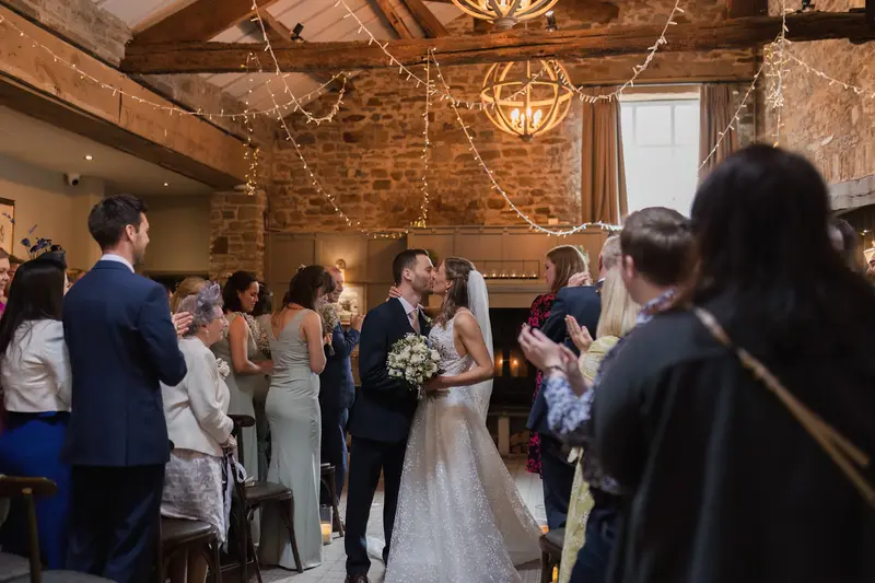 Wide angle documentary wedding first kiss photo inside rustic Yorkshire barn venue