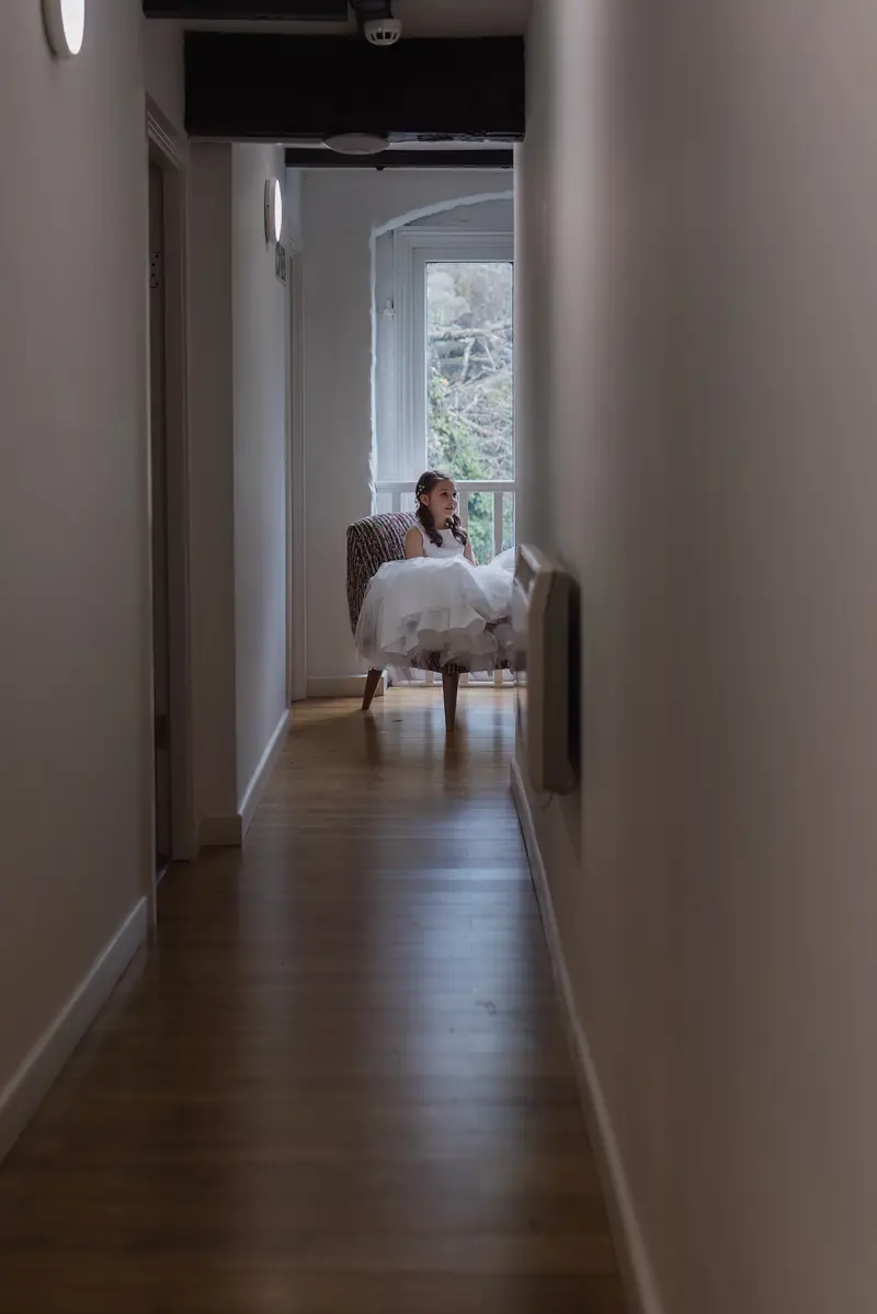 Flower girl sitting by window in cinematic wedding morning preparation photograph