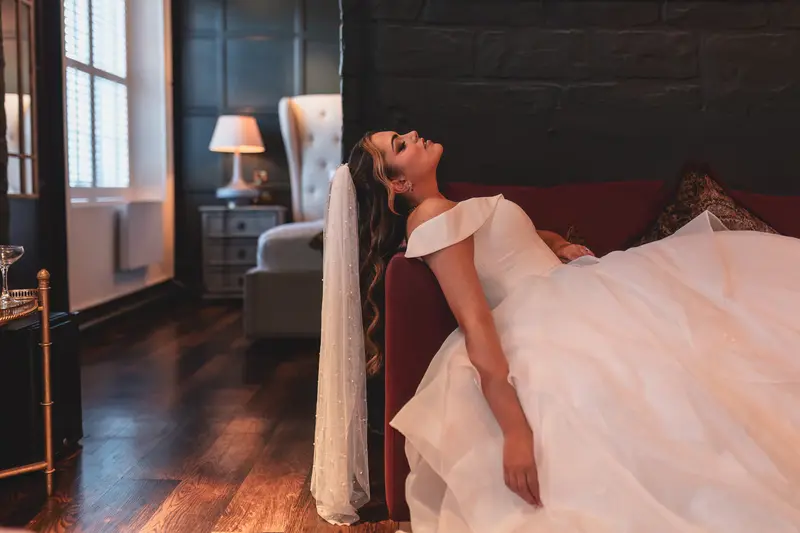Creative bridal portrait relaxing on a sofa during elegant wedding morning preparations