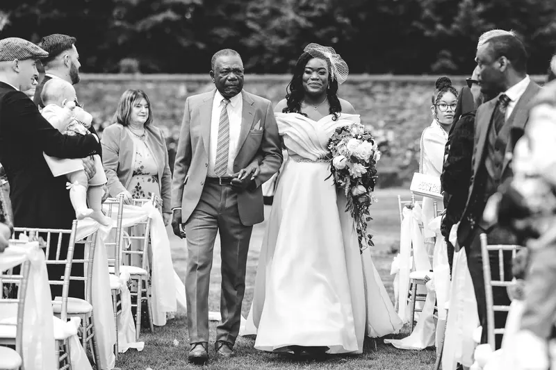 Black and white photo of bride walking down the aisle during outdoor wedding ceremony