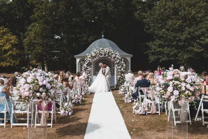 Romantic wedding kiss under floral gazebo during outdoor ceremony