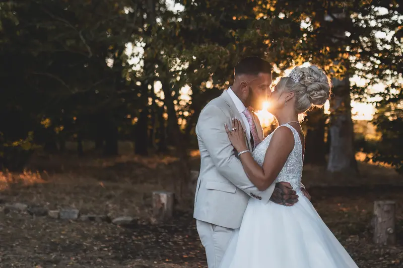 Sunset wedding kiss with cinematic golden light through trees