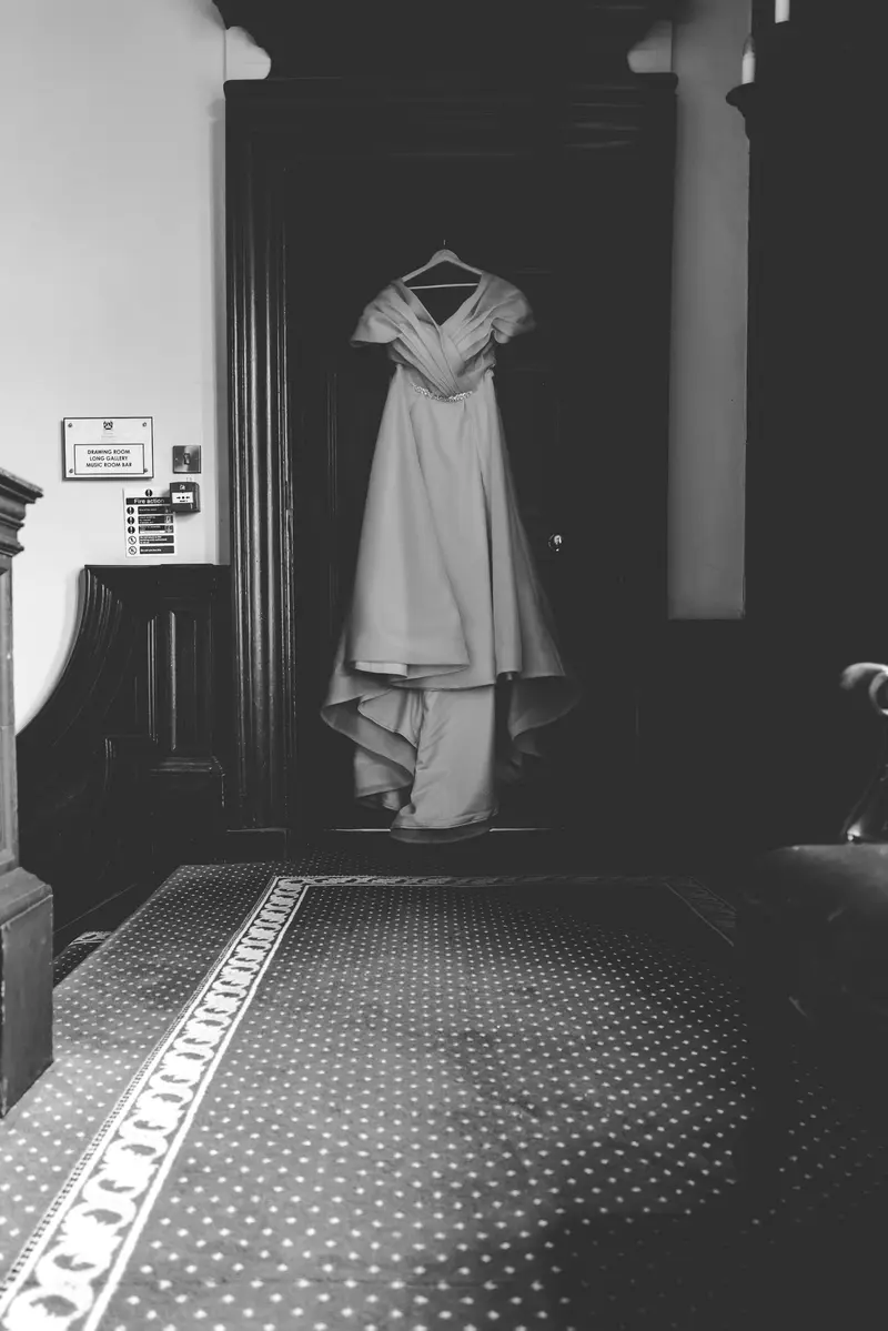 Black and white bridal portrait with wedding dress hanging in the preparation room