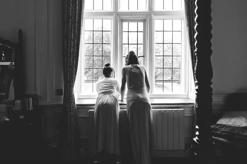 Black and white documentary photo of bridesmaids looking out of the window before the ceremony
