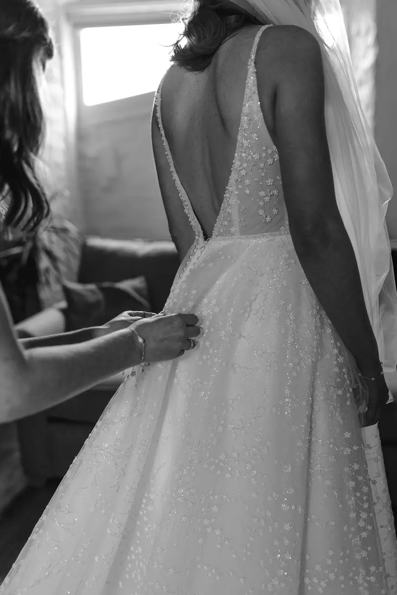 Elegant black and white bridal preparation photo of wedding dress fastening with cinematic documentary style