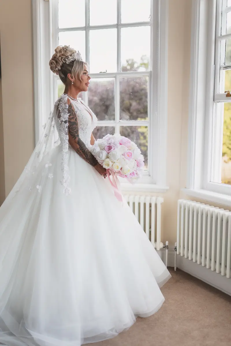 Bride holding pastel bouquet by window, natural light bridal portrait, cinematic wedding photography