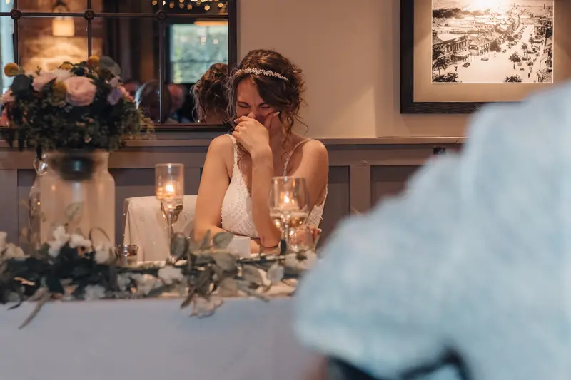 Emotional bride reaction during wedding speeches at intimate reception