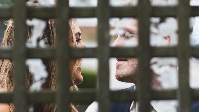 Creative framed portrait of the bride and groom through a garden fence