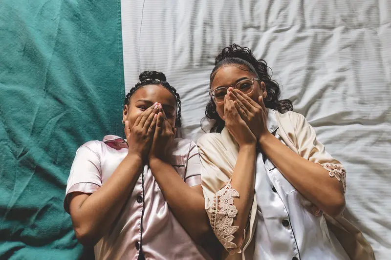 Bridesmaids laughing together on the bed during relaxed wedding morning preparations