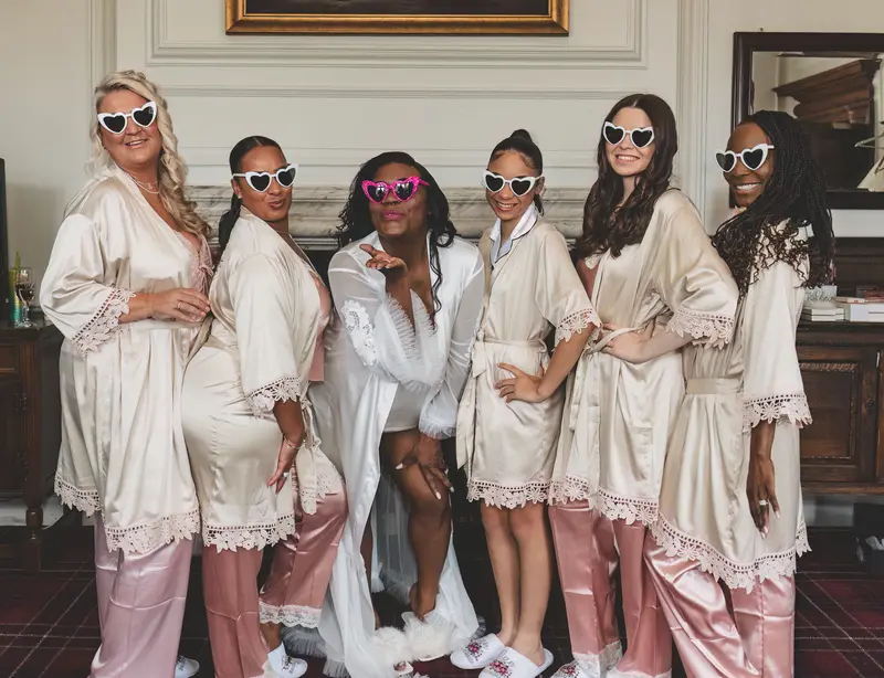 Bride and bridesmaids celebrating in robes and sunglasses before the wedding ceremony