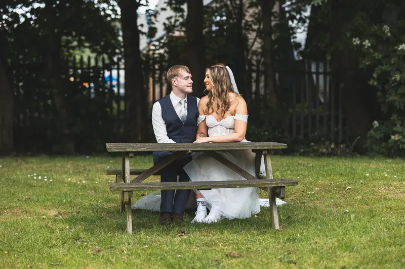 Bride and groom sitting together on a picnic bench during outdoor wedding portraits