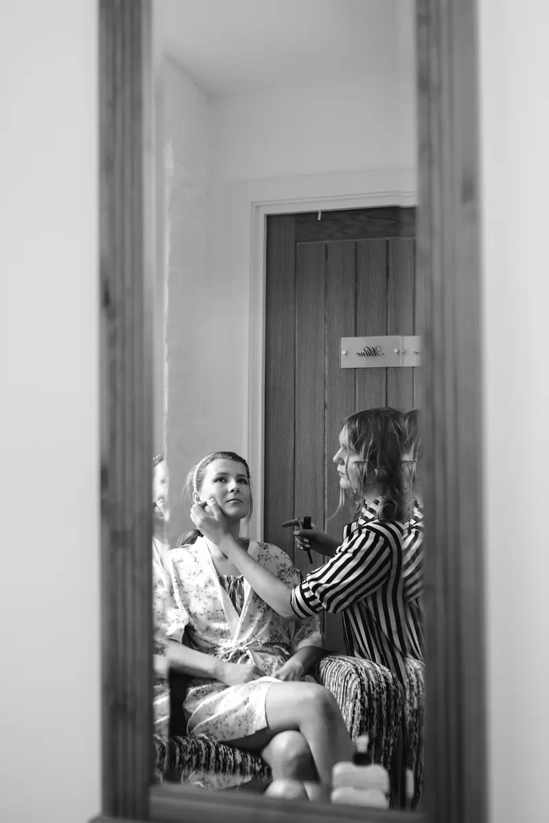 Black and white mirror reflection of bride having makeup applied before wedding ceremony