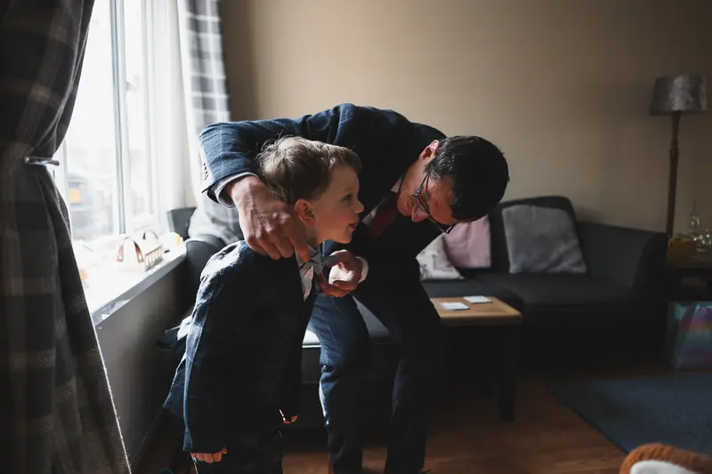 Groom helping young boy with bow tie during wedding preparations