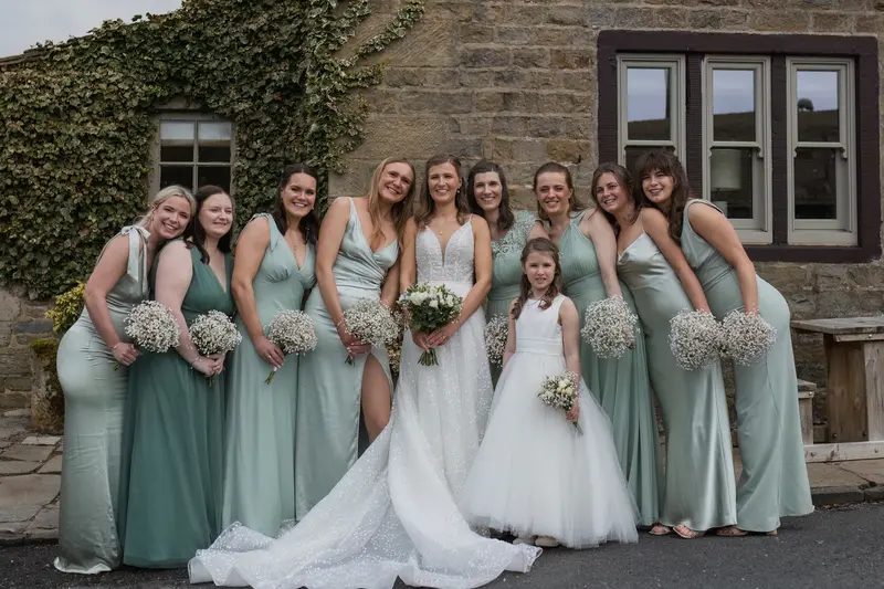 Natural bridal party portrait at Yorkshire wedding venue with bride, bridesmaids and flower girl in sage green dresses