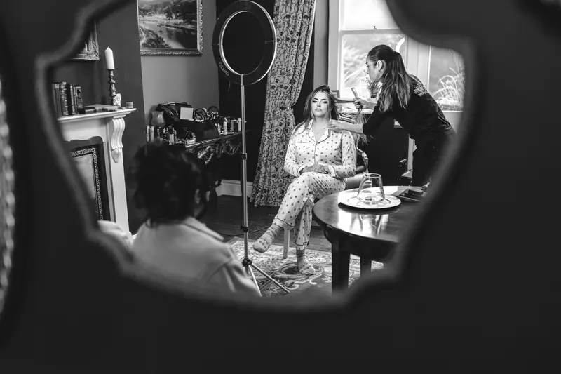 Bride having her makeup applied, reflected in a decorative mirror during bridal preparations
