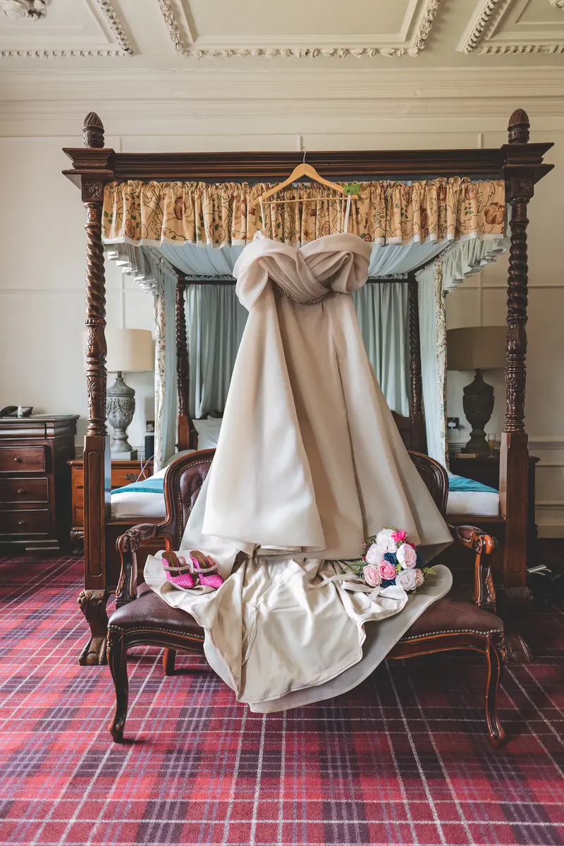 Wedding dress hanging above bridal shoes and flowers in a historic bridal suite