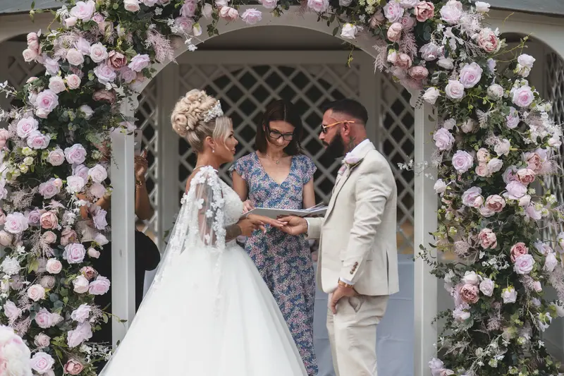 Bride and groom exchanging rings under floral arch, elegant outdoor wedding ceremony UK