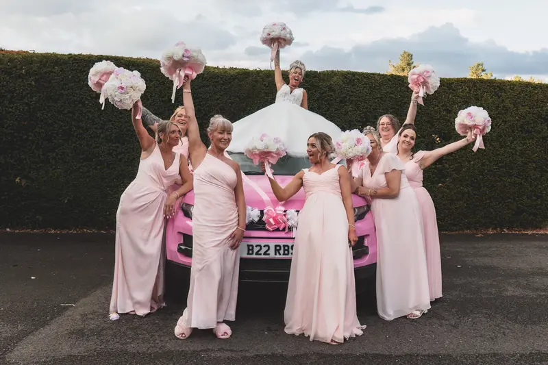 Fun bridal party photo with pink wedding car and bridesmaids celebrating