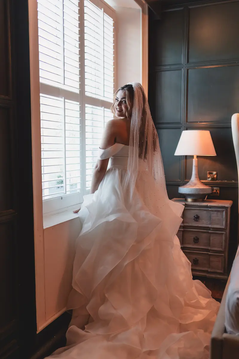 Bride smiling beside the window during natural light bridal portraits before the ceremony