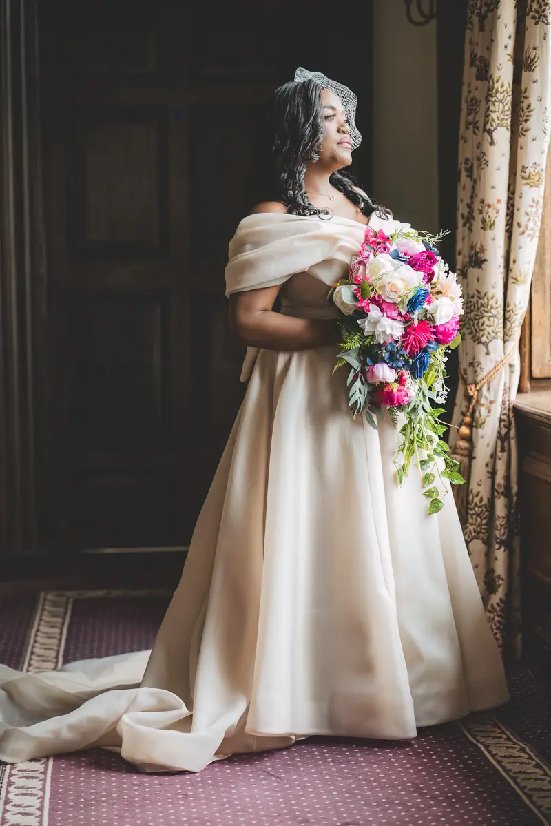 Bride holding her colourful bouquet beside a window during bridal portraits