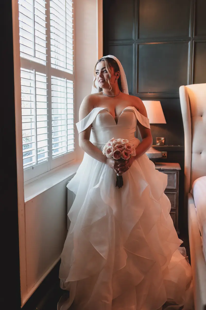 Elegant bridal portrait holding her bouquet beside a window before the wedding ceremony