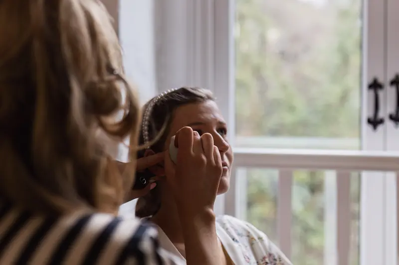 Bride getting makeup done by window during natural light wedding preparations in Yorkshire