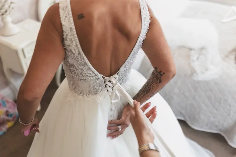 Bride getting wedding dress laced up, emotional bridal preparation photography, documentary wedding moments