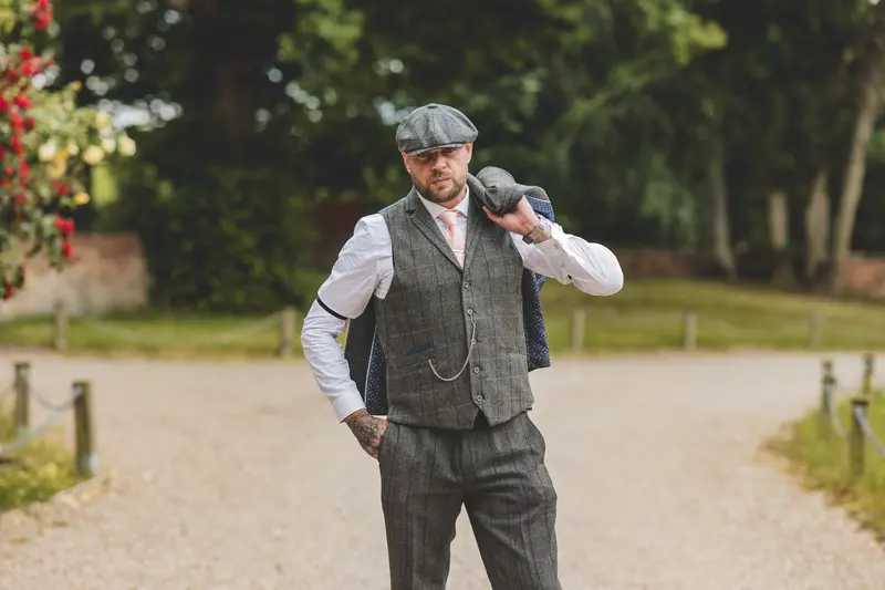 Groom adjusting his flat cap during stylish outdoor wedding portraits