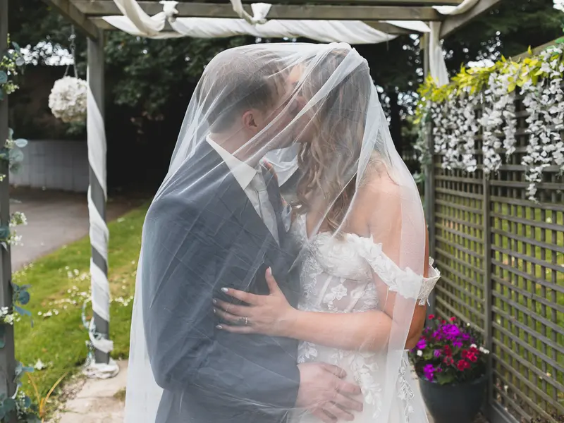 Close up wedding portrait of the couple sharing a kiss beneath the veil