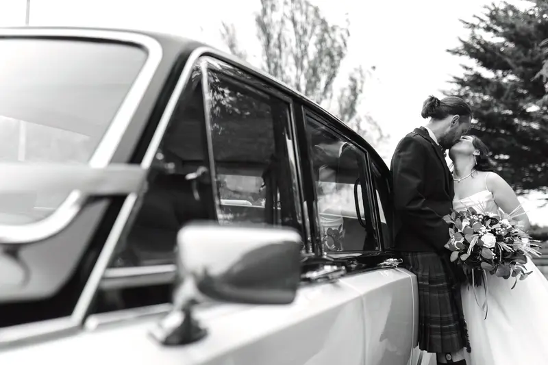 Black and white wedding portrait beside vintage car, artistic documentary wedding photographer UK