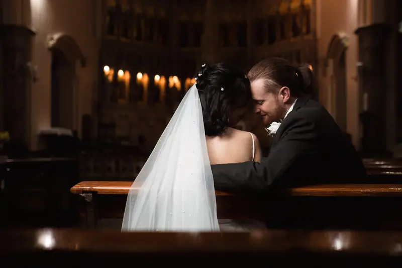 Intimate newlywed moment inside church pews, dark and moody wedding photography Yorkshire