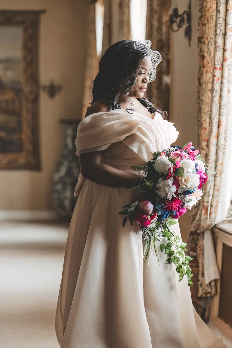 Bride standing by the window holding her bouquet before the wedding ceremony