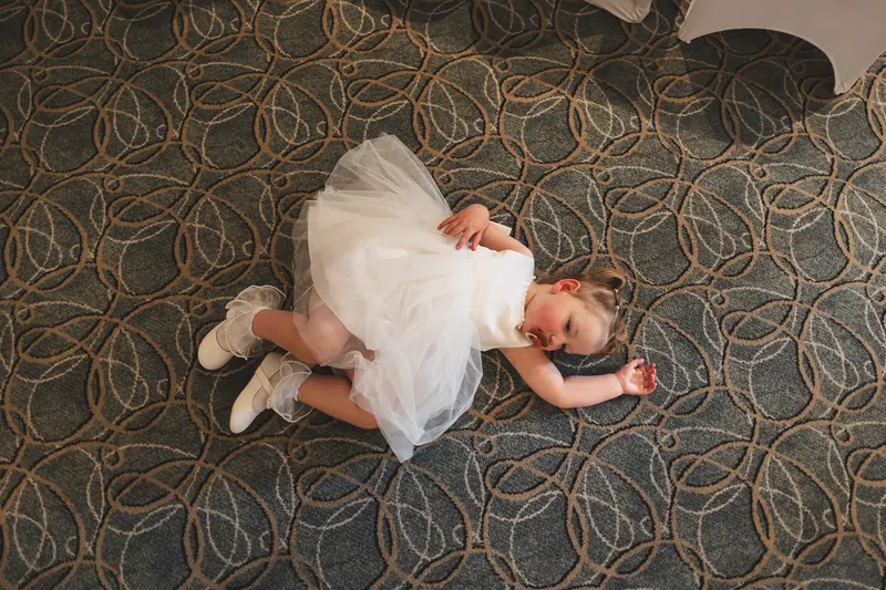 Flower girl lying on the floor in her white dress during a candid documentary wedding