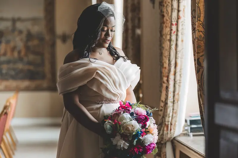 Bride holding her colourful bouquet during elegant window light bridal portraits