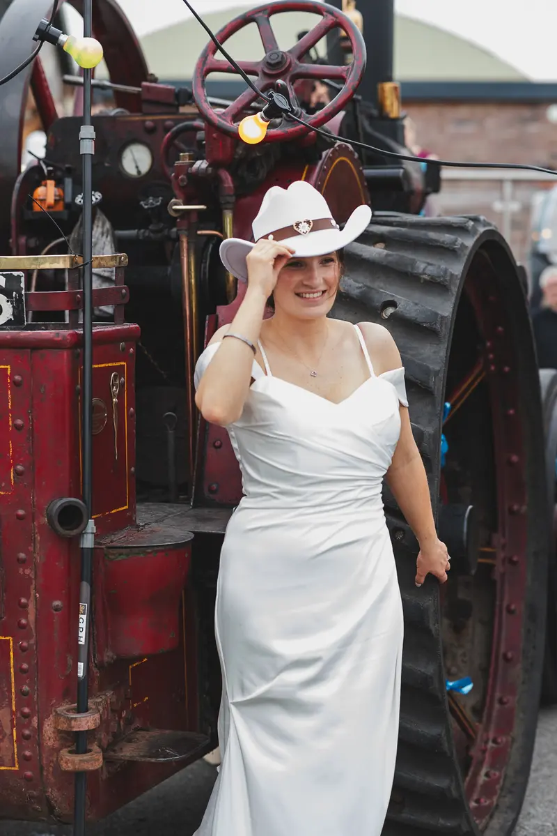 Bride portrait with cowboy hat beside vintage steam tractor