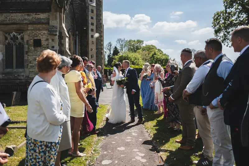Newlyweds kissing outside church surrounded by wedding guests in Yorkshire