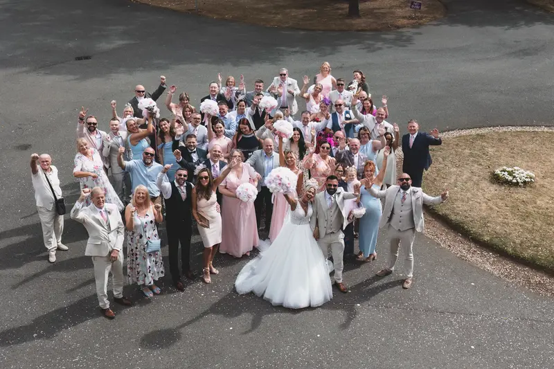 Fun aerial wedding group photo with guests celebrating outside venue
