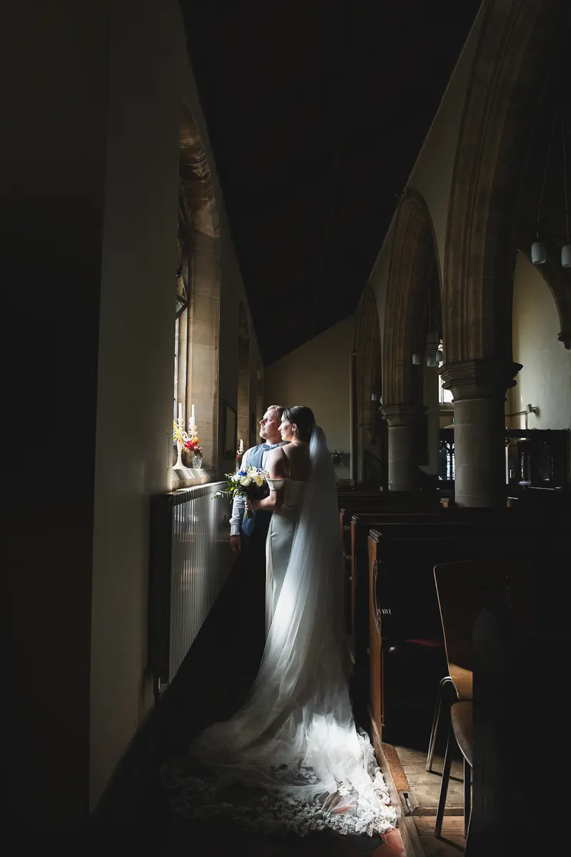 Cinematic church wedding portrait with long bridal veil and dramatic shadows