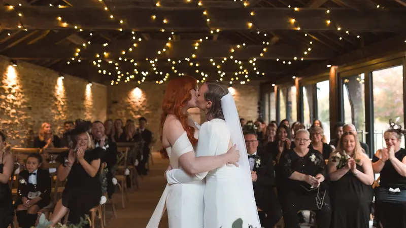 Romantic first kiss during lesbian wedding ceremony with emotional guests