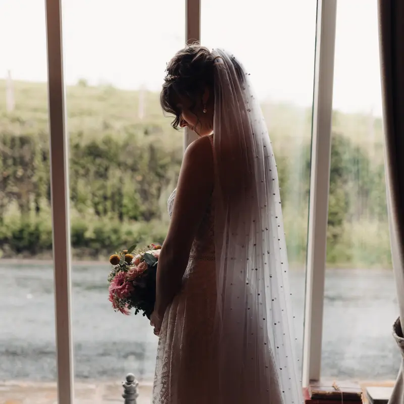 Romantic bridal portrait with veil and bouquet by countryside window light