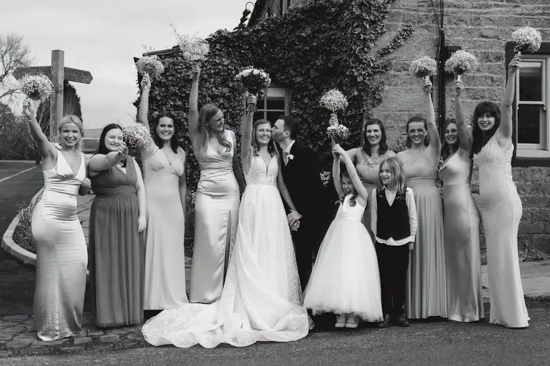 Black and white documentary wedding group photo with bride and groom celebrating with bridesmaids and flower girls in Yorkshire