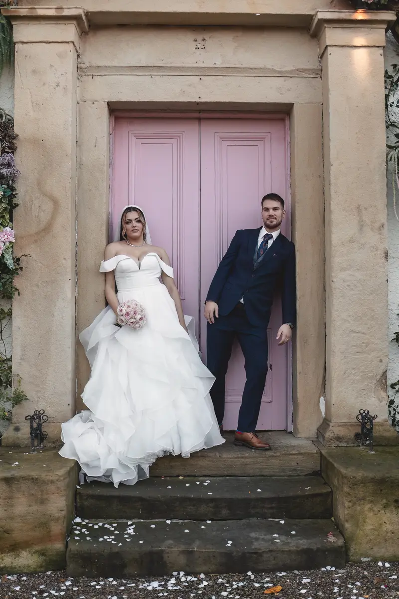 Bride and groom posing naturally outside the wedding venue with elegant pink doors