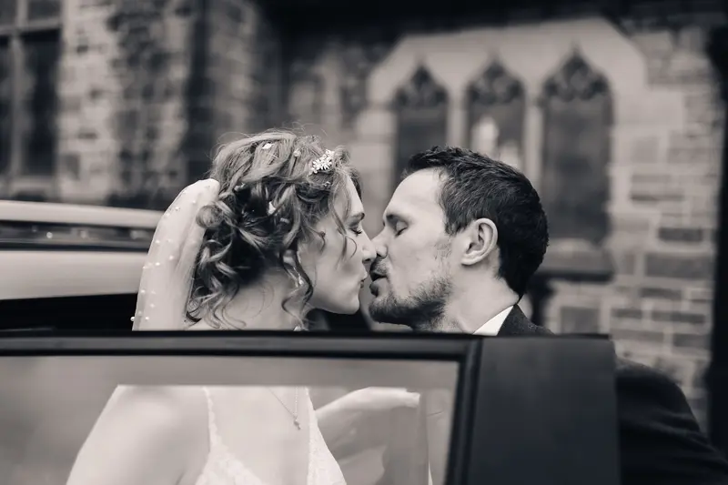 Black and white cinematic wedding kiss through car door reflection