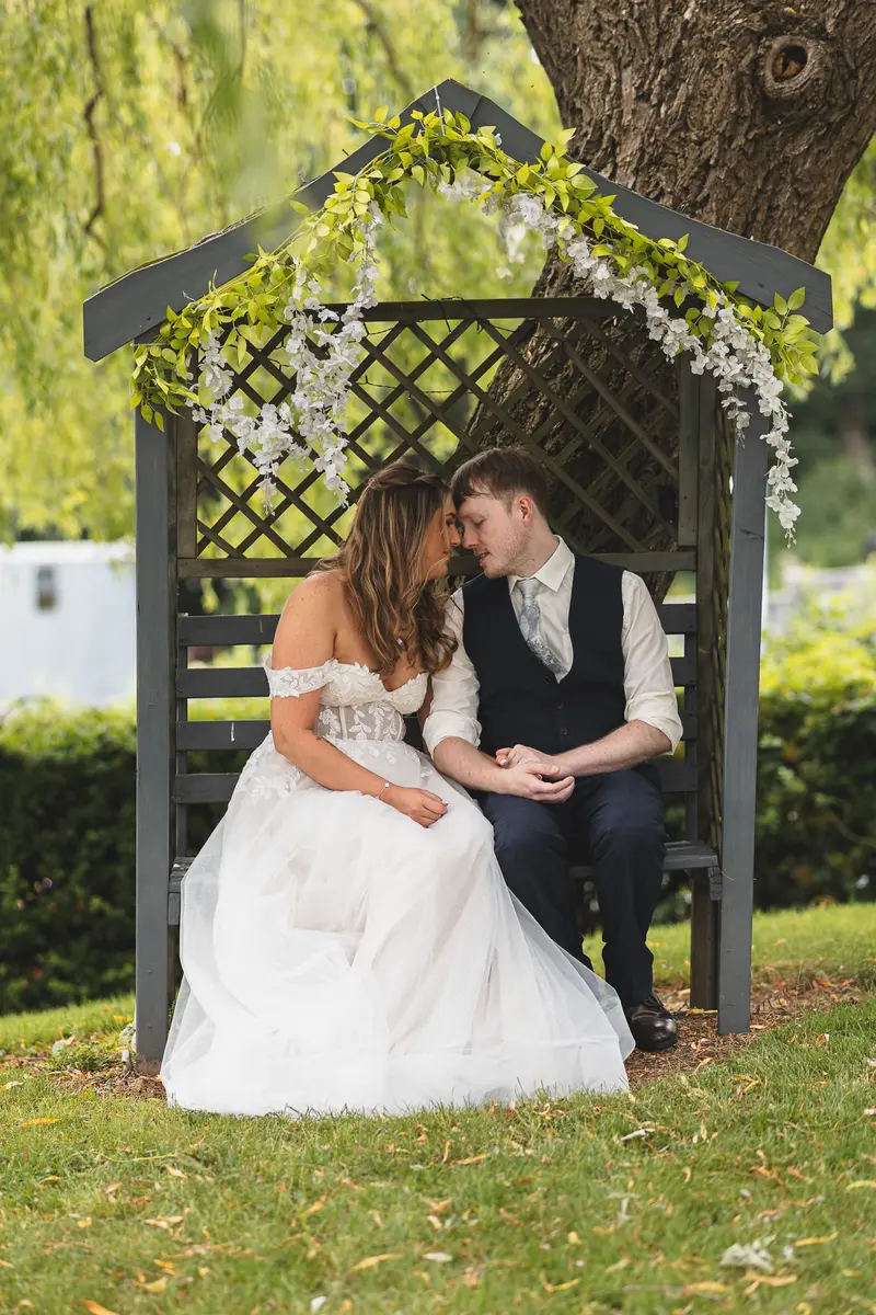Bride and groom cuddling beneath a wooden garden arch during romantic portraits