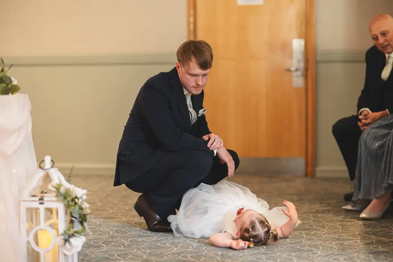 Candid moment of the groom checking on a flower girl during the wedding ceremony, captured with natural documentary wedding photography